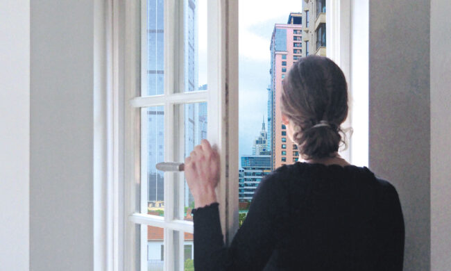 Projekt Offene Fenster – Was Fenster über mein Land erzählen. Frau schaut aus Kleinstadtfenster hinaus in die große Stadt