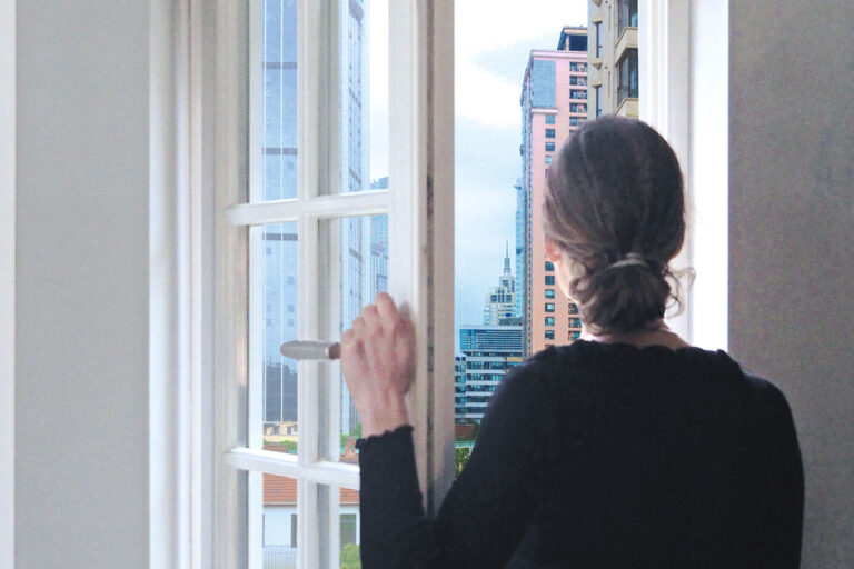 Projekt „Offene Fenster – Was Fenster über mein Land erzählen.“ Projekt Offene Fenster – Was Fenster über mein Land erzählen. Frau schaut aus Kleinstadtfenster hinaus in die große Stadt